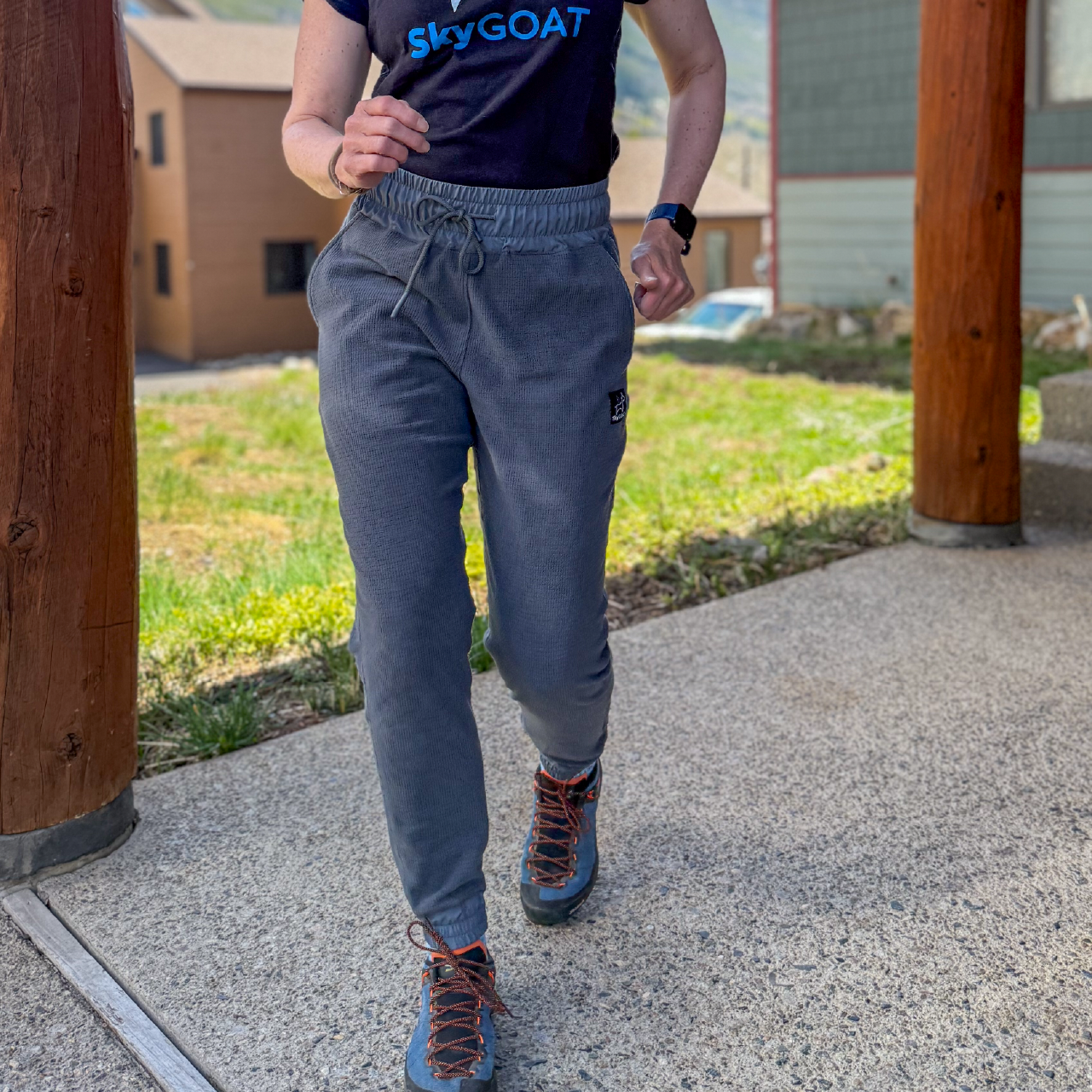 Person wearing SkyGOAT Women's Microgrid Fleece Jogger Pants in walking on a concrete path with a wooden structure and grassy area in the background.